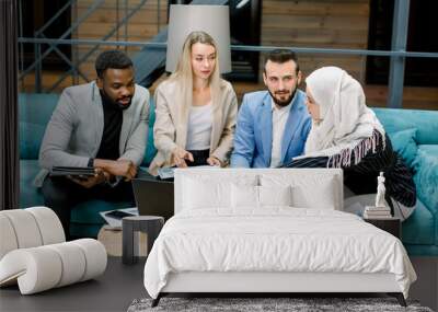 Close up of four smart young multiracial business partners, two men and two women, brainstorming with one another, discussing ideas and business project in fashionable office room Wall mural