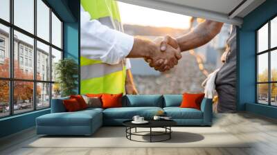 Close up of two strong roof inspectors doing hand shaking while standing during sunset on open air. Responsible male workers concluding deal and agreeing on cooperation together outdoors. Wall mural