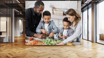 Close up view of parents and their sons cooking in kitchen preparing food salad together. Happy boys children assist mom and dad, helping with dinner or lunch, tearing leaves of lettuce into bowl. Wall mural