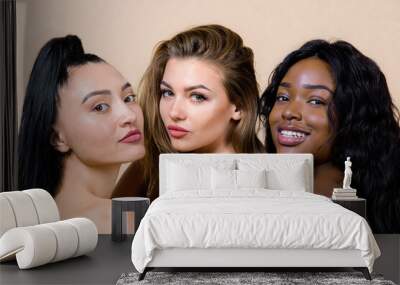 Ethnic diversity. Beauty close up portrait of three charming young multiracial women, Asian, Caucasian and African, with nude makeup and perfect skin, standing together against beige background Wall mural