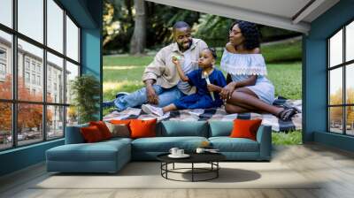 Family, parenthood and people concept. Happy smiling African family, father, mother and cute girl child in the park together on a sunny day, blowing soap bubbles Wall mural