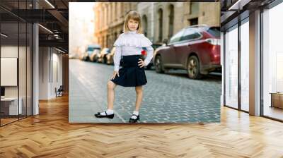 Full length portrait of beautiful little blond girl outdoors at old city street in Lviv, Ukraine. Fashion strret portrait of pretty girl in the city Wall mural