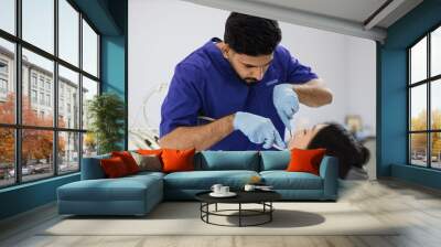 Happy patient and dentist concept. Young bearded asian male stomatologist treating teeth of a beautiful asian woman patient, using tooth drill. Oral health and hygiene. Wall mural