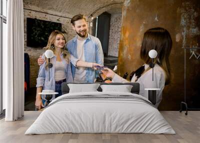 Happy smiling couple giving their reservation details and passports to a concierge while checking in together at the reception counter of a hotel Wall mural