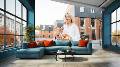 Happy smiling young business woman eating salad on lunch break in city street, healthy living lifestyle. Healthy eating nutrition concept. Wall mural