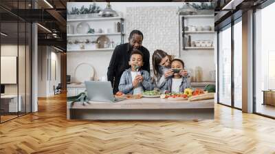 Happy young multiracial family with two little kids have fun cooking healthy breakfast in kitchen together. Excited parents with small children prepare diet vegetarian salad in own home in the morning Wall mural