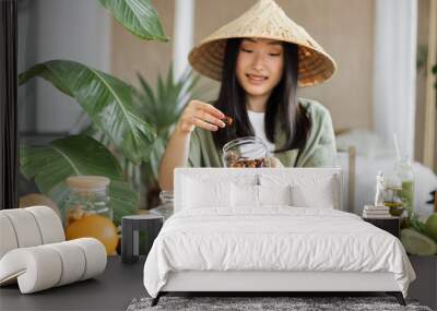 Healthy food to boost your immune system. Beautiful smiling asian young woman blogger in traditional conical hat cooking fresh organic healthy food using dates indoor at exotic tropical home studio Wall mural