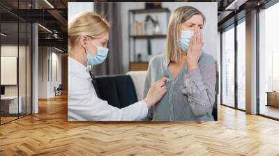 Home treatment of virus infection, coronavirus pandemic, Covid-19 outbreak. Female doctor during home visit examining sick senior woman patient in face mask, coughing, having chest pain. Wall mural