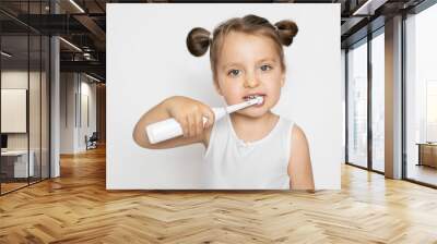 Little cute blond girl brushing her teeth with electric toothbrush. Oral teeth care and caries prevention. Close up horizontal studio shot on isolated white background Wall mural