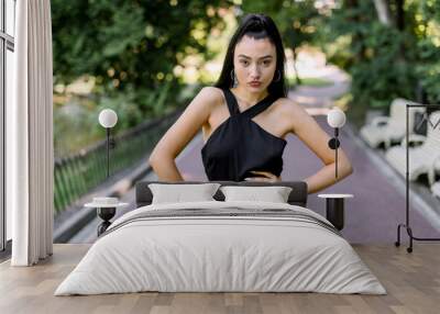 Outdoor portrait of attractive young Asian mixed raced girl with black ponytail hair, wearing elegant fashionable black clothes, posing to camera, posing in the green park alley Wall mural