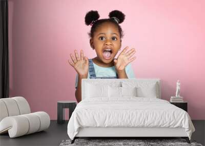 Portrait of surprised screaming cute little African girl child standing isolated over pink background, looking at camera with open mouth. Concept of children's emotions, facial expression Wall mural