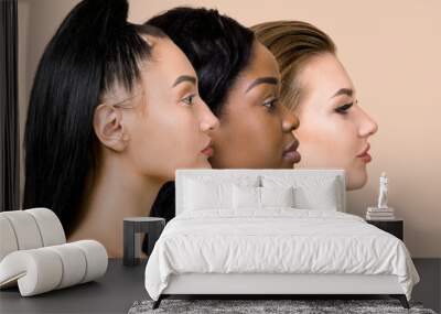 Profile close up portrait of three beautiful multiracial women, Asian, African and Caucasian, with different types of skin and hair, posing over beige background. Natural beauty of women. Copy Space Wall mural