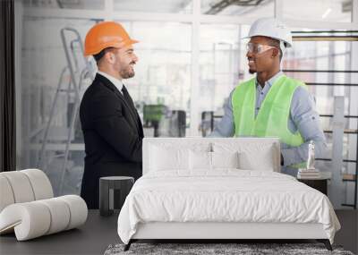 Side view of caucasian and afro-american men in helmets shaking hands after successful meeting on construction. Two partners enjoying international cooperation. Wall mural