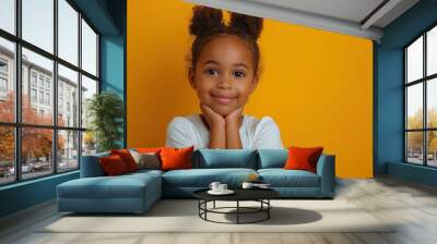 Smiling young girl posing with hands on chin against yellow background Wall mural