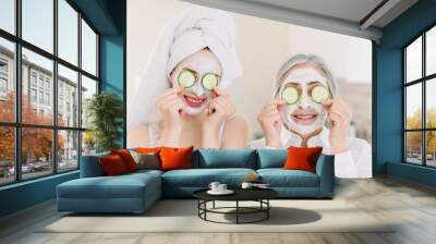 Spa and wellness. Anti age mask. Skin care for all ages. Ssmiling attractive senior gray haired woman with her granddaughter making clay facial masks and covering eyes with cucumber slices Wall mural