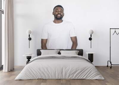 Young and handsome. Handsome young African man in casual tshirt holding hands in pockets and smiling while standing against white background Wall mural