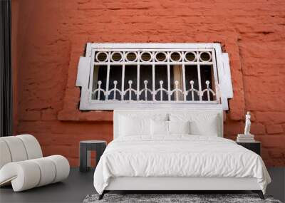 A small white window with bars on the red brick facade Wall mural