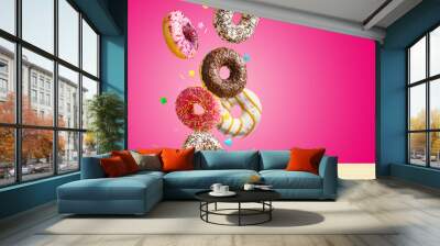 Flying donuts. Mix of multicolored sweet doughnuts with sprinkel on pink background falling on the table. Wall mural