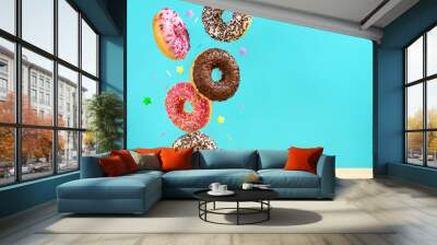 Flying donuts. Mix of multicolored sweet doughnuts with sprinkel on turqouise blue background falling on the table. Wall mural