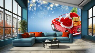 Santa Claus driving red car with gift boxes and Christmas tree on blue background with bokeh lights Wall mural