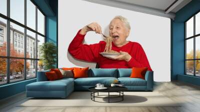 Happy senior woman eating italian spaghetti pasta isolated on white studio background Wall mural