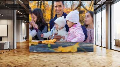 big family has picnic in autumn city park, children and parents sitting together at the table, with apples and yellow maple leaves, happy people enjoying beautiful nature, bright sunny day Wall mural