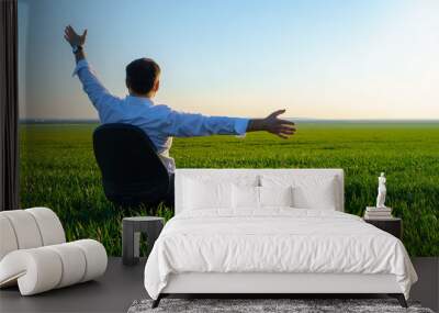 businessman sits in an office chair in a field and rests, freelance and business concept, green grass and blue sky as background Wall mural