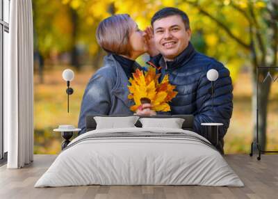 portrait of a romantic couple in an autumn city park, a man and a woman posing, they hold yellow leaves and kiss, a bright sunny day Wall mural