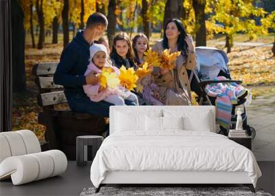 portrait of big family with children in an autumn city park, happy people sitting together on a wooden bench, posing and smiling, beautiful nature, bright sunny day and yellow leaves Wall mural