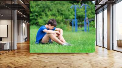 teenage boy exercising outdoors, sports ground in the yard, he sits on the green grass of the playground, healthy lifestyle Wall mural