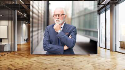 Senior businessman wearing eyeglasses standing in front of corporate office building and thinking Wall mural