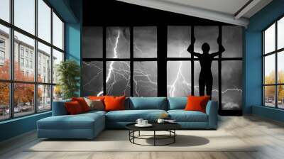 Silhouette of man watching lightning, thunder, rain and storm through the broken window of abandoned building Wall mural