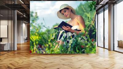 Young beautiful elegant woman reading book on the sunny summer meadow Wall mural