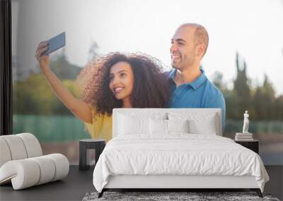 Black woman and white man, cheerful and happy couple taking a selfie shot in a city. Wall mural