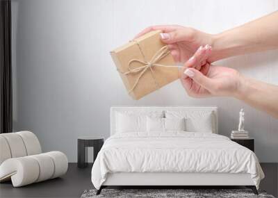 Hands of a young girl holding a gift box. Cardboard box tied with twine. Light back. Wall mural