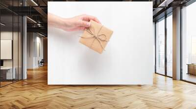 The hand of a young girl holding a gift box. Cardboard box tied with twine. Light background. Wall mural