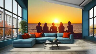 Group of friends enjoying a sunset on the beach while sitting together on warm sand, capturing a moment of tranquility and togetherness Wall mural