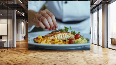 Close up of a female chef hands plating fish with pasta and vegetables on a white plate in a restaurant, with a focus on the hands Wall mural