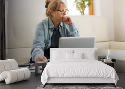 Active mature woman using a laptop for remote work from the home office. Video conference, video meeting. Senior teacher leads webinar Wall mural