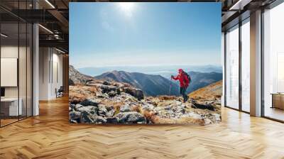 Backpacker woman in bright red jacket walking by mountain range using trekking poles with Liptov valley background, Western Tatras, Slovakia. Active people and European hiking tourism concept image. Wall mural