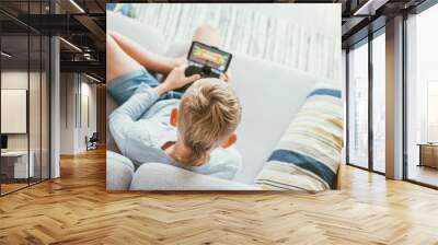 Boy sits on sofa plays with smartphone and gamepad camera top view. Child and electronic devices concept Wall mural