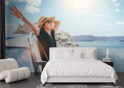 Cheerful Woman portrait enjoying the seaside road trip. Dressed a black dress, straw hat and sungllasses she wide opened arms and shining with happiness. Summer vacation traveling by auto concept. Wall mural