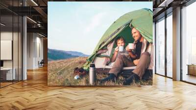 Family lisure concept image. Father and son drink a tea sitting in touristic tent Wall mural