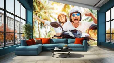 Happy smiling couple travelers riding motorbike scooter in safety helmets during tropical vacation under palm trees Wall mural