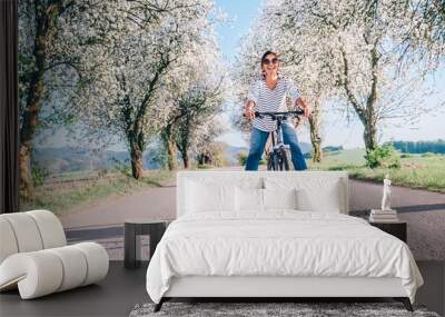 Happy smiling woman rides a bicycle on the country road under the apple blossom trees Wall mural