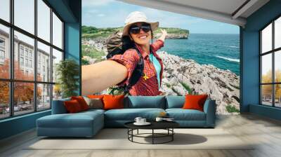 Happy woman backpacker traveler take a selfie photo on amazing ocean coast Wall mural