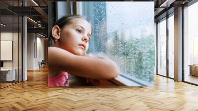 Little sad girl pensive looking through the window glass with a lot of raindrops. Sadness childhood concept image. Wall mural