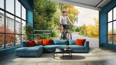 Portrait of a happy smiling man dressed in cycling clothes, helmet and sunglasses riding a bicycle on the asphalt out-of-town bicycle path. Active sporty people concept image. Wall mural