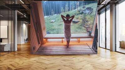 Relaxing Woman wrapped white towel in Hot Finnish sauna with a huge wide window enjoying the green forest view and pleasant healthy body care temperature treatment. Body healthcare prevention concept Wall mural