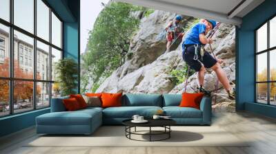 Smiling teen boy in protective helmet abseiling from cliff rock wall using rope, Belay device and climbing harness with father in Paklenica Park Croatia. Active extreme sports time spending concept Wall mural